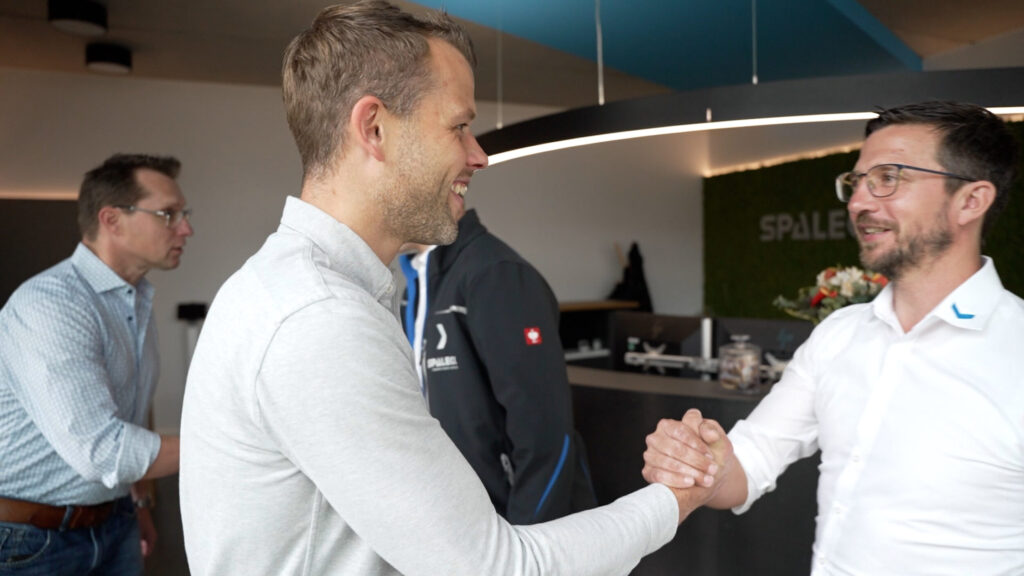 Two men shake hands with a smile in a modern office.