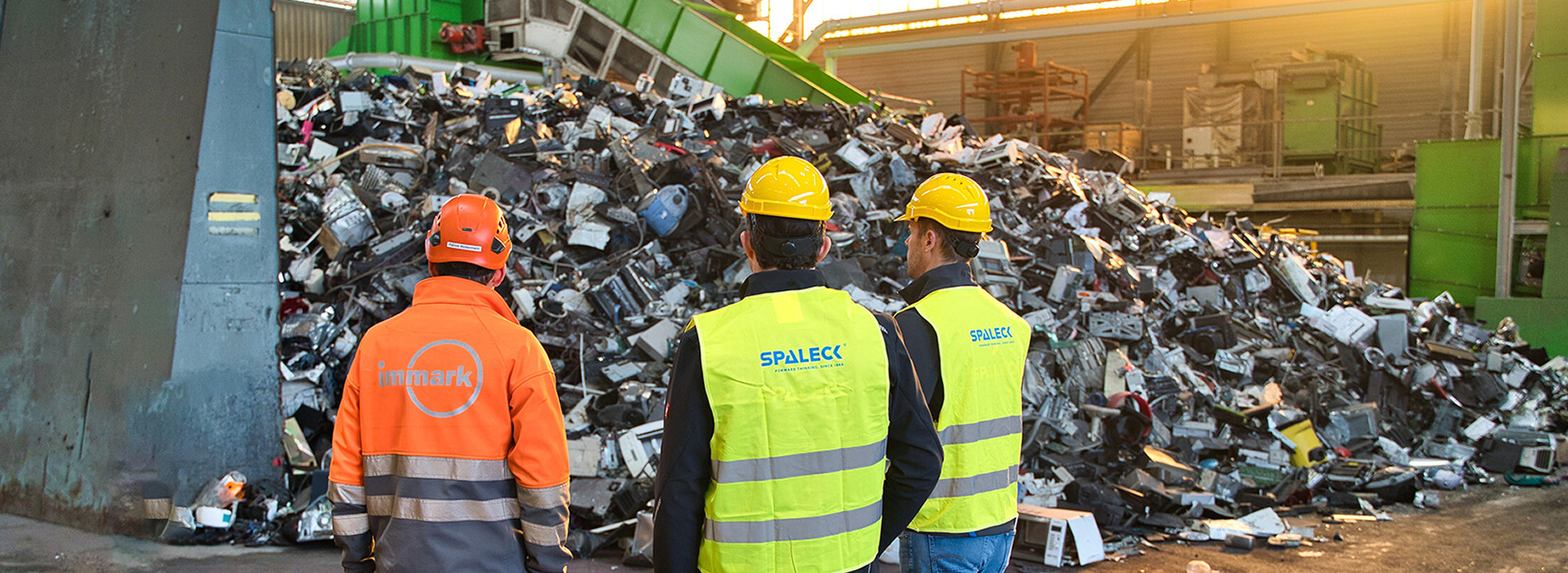 Workers standing in front of a large pile of electronic waste at a recycling plant.