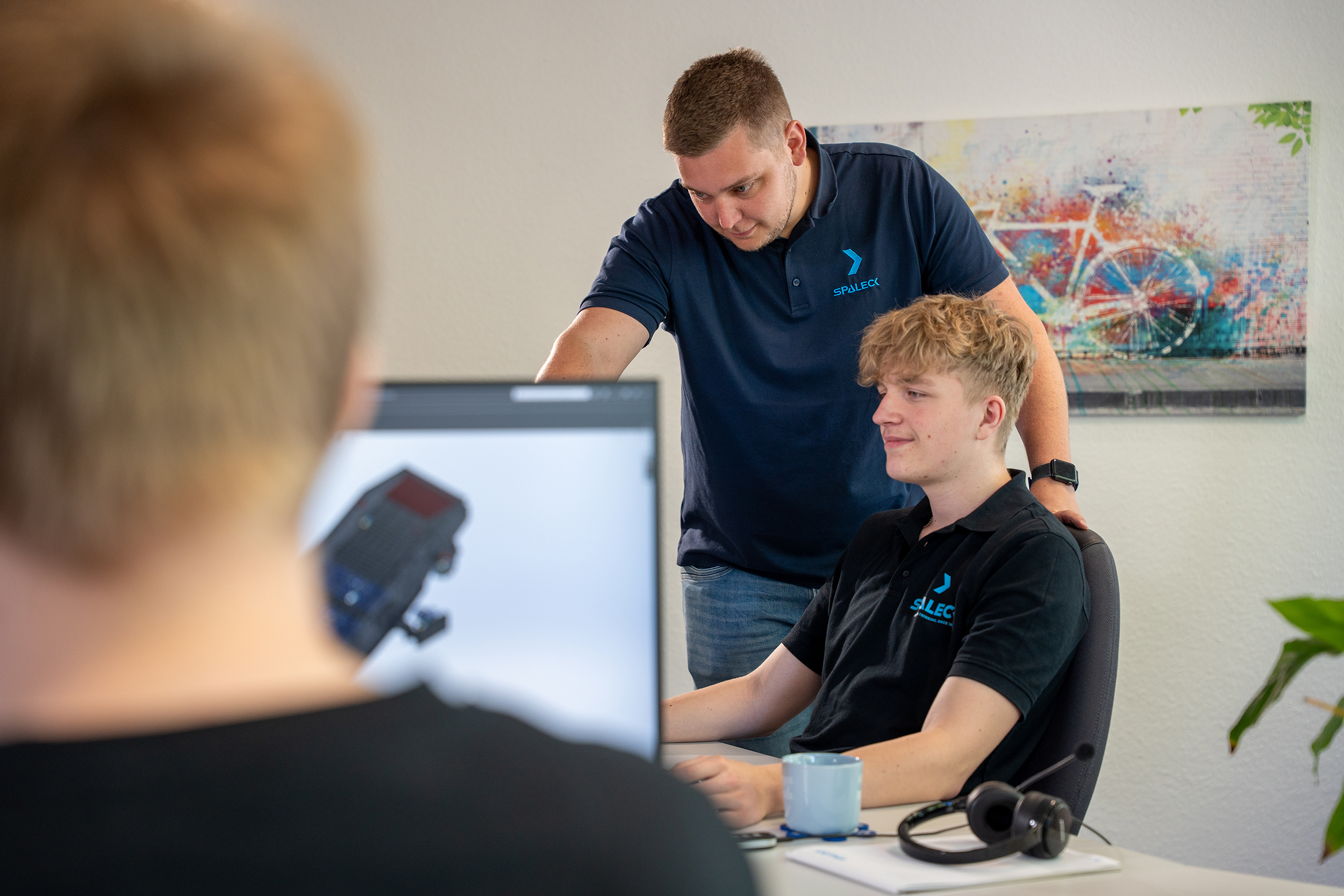 A coworker shows a technical product design apprentice something on the screen
