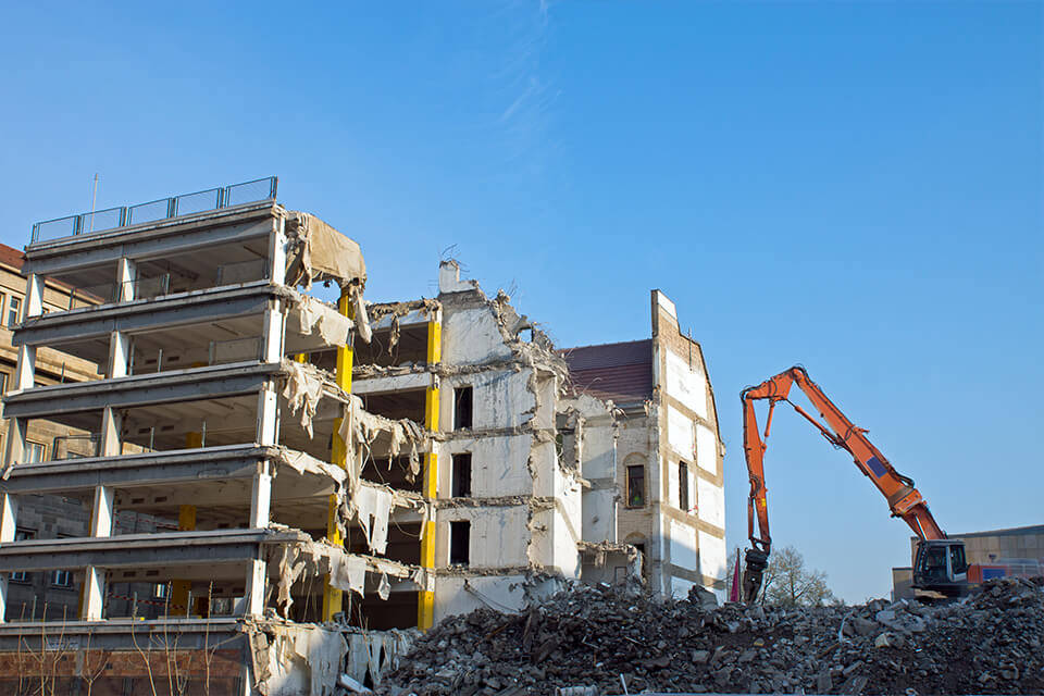 Demolition of a building using an excavator, with construction debris in the foreground.