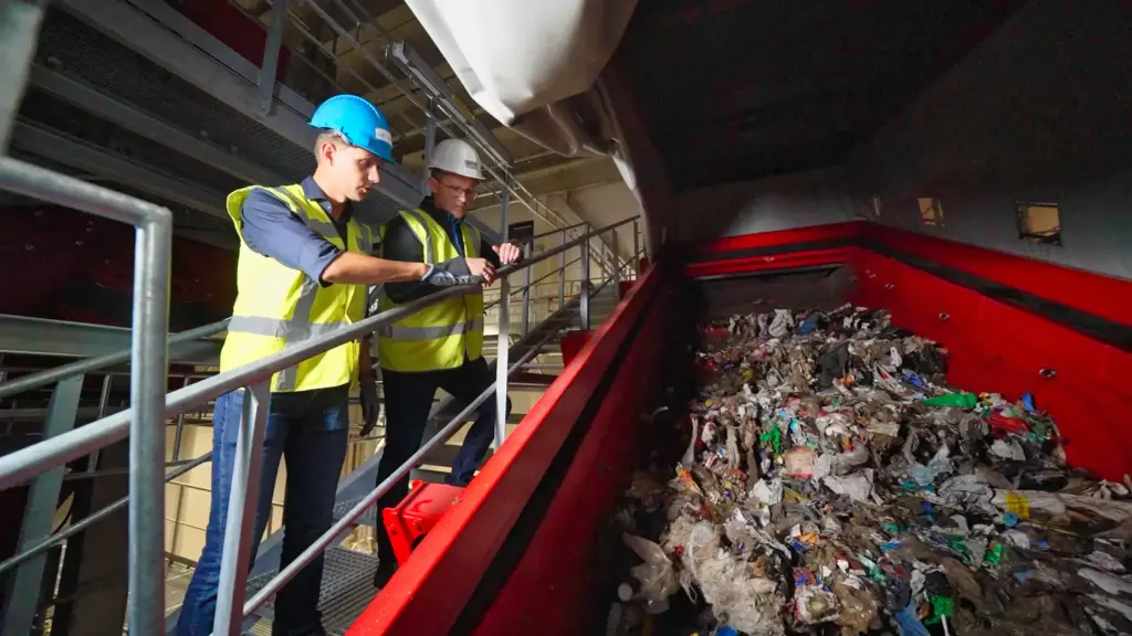 Two recycling experts are looking at a SPALECK screening machine at a large household waste recycling facility.