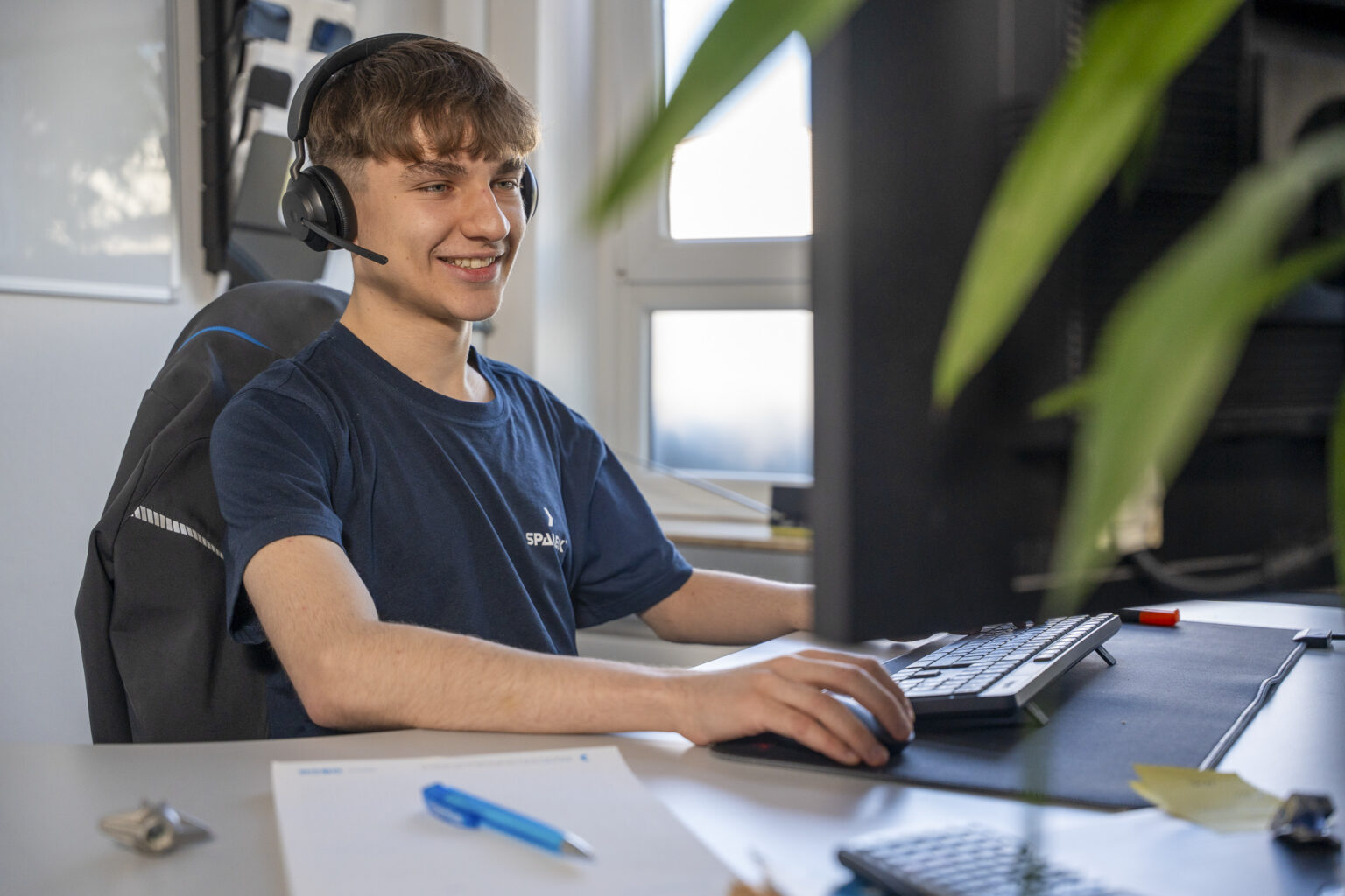 An industrial business administration apprentice is sitting at a desk and talking on the phone with a headset