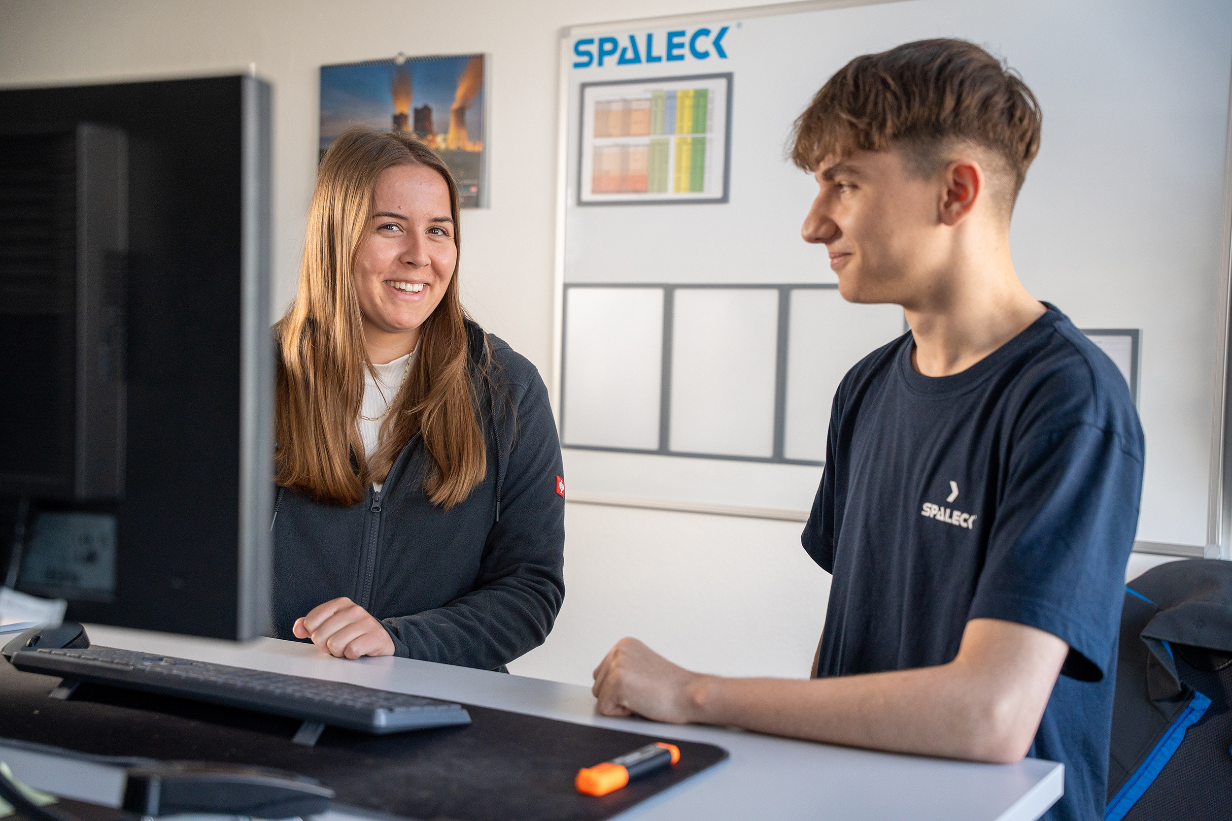 Two industrial business administration trainees are talking at their desk