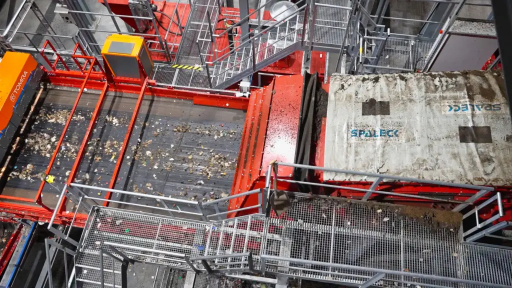 A tension-shaft screening machine (Flip-Flow screen) located upstream of a sorting machine at a household waste recycling facility. The SPALECK tension-shaft screening machine produces precisely screened material. Screening out the fine particles helps ensure that the subsequent sensor sorting (Tomra Machine) can function optimally.