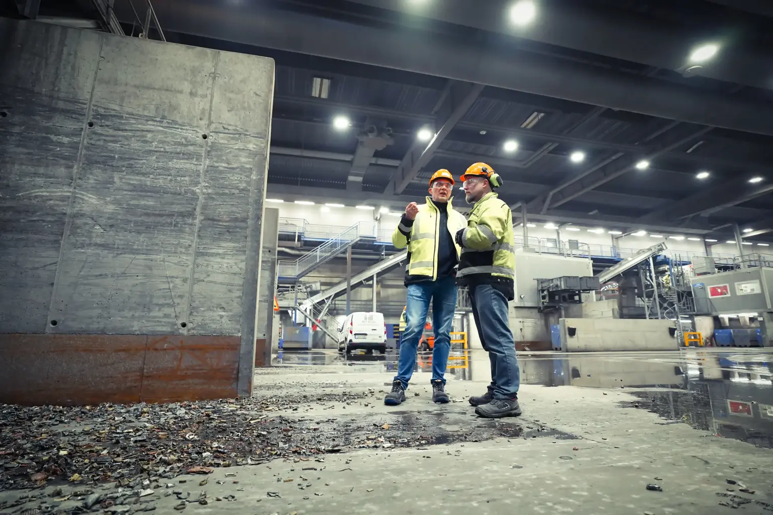 Two workers in protective gear are talking in an industrial building.
