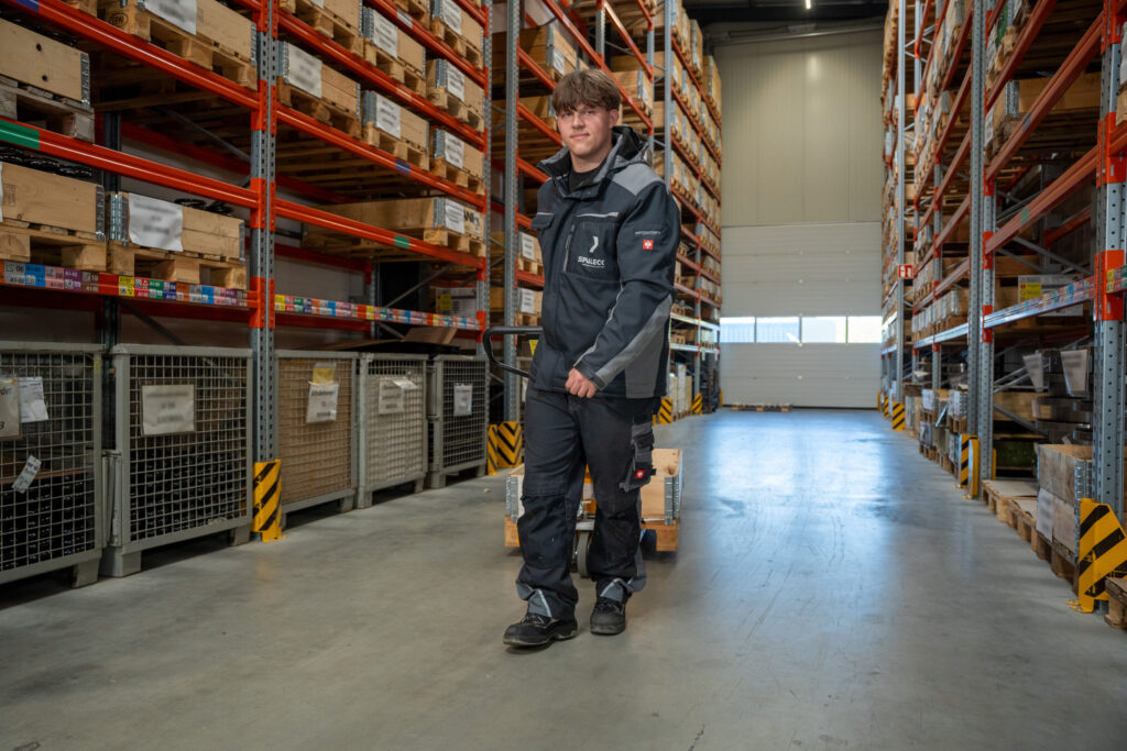 An apprentice warehouse logistics specialist pushes a pallet jack through the warehouse