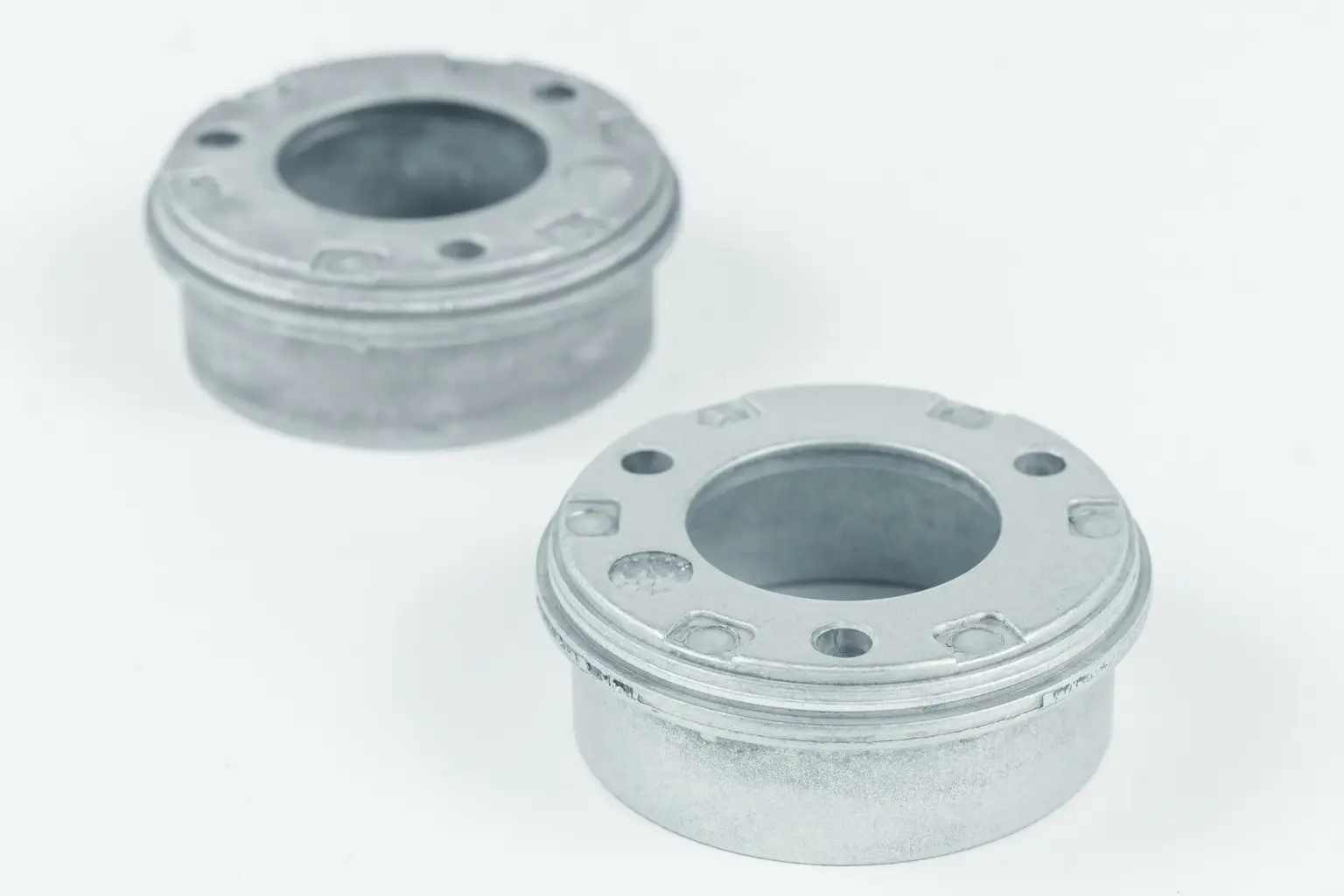 Two metal components with round openings on a light-colored background.