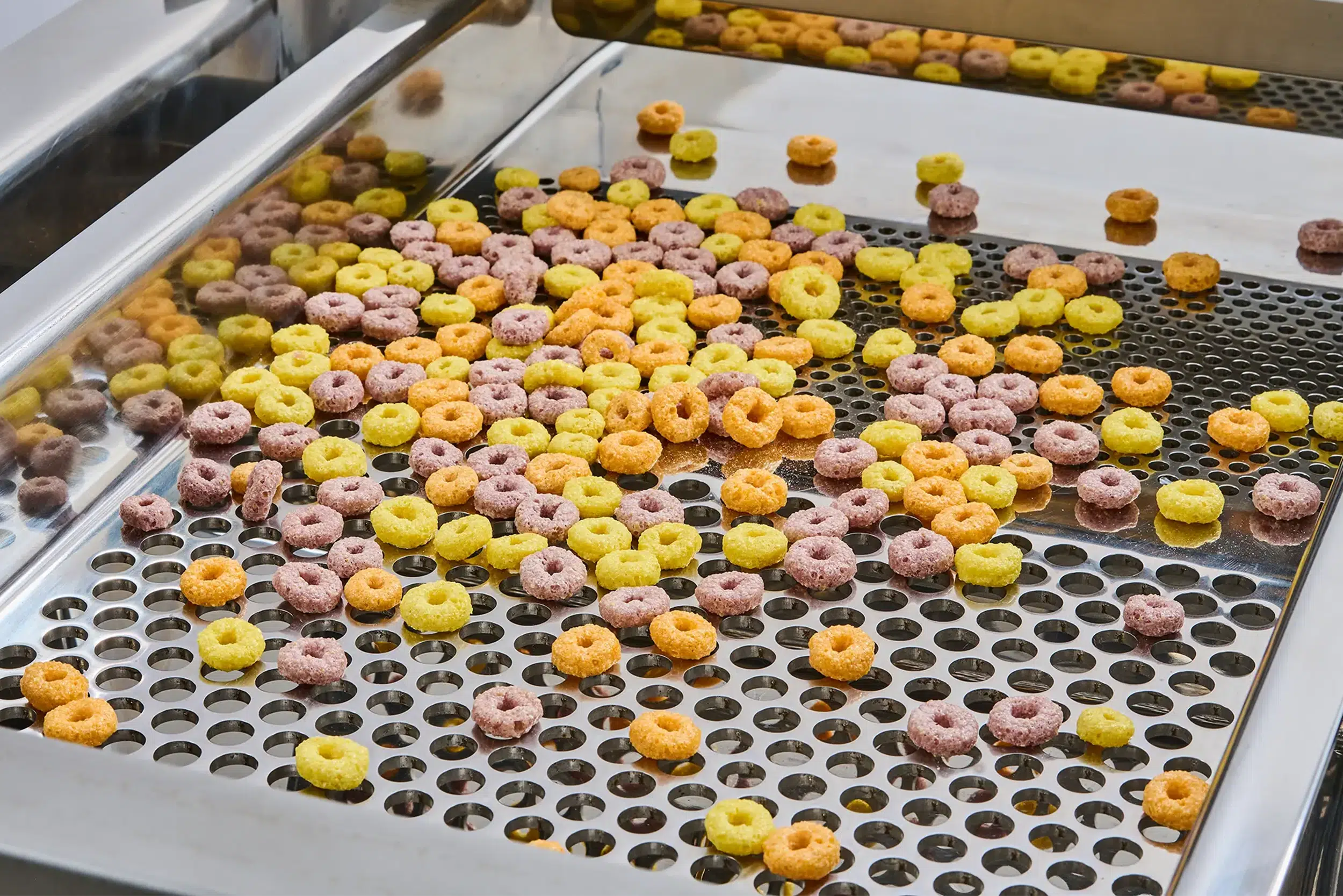 Food-processing sieves separate colorful cereal rings on a sieve.