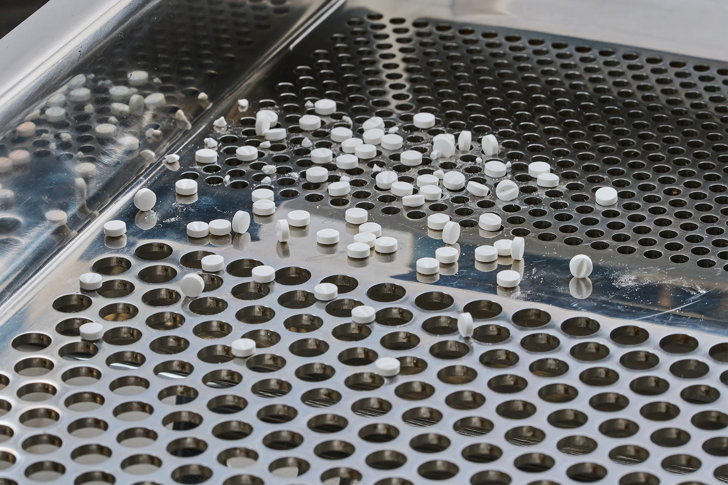 White tablets on a metal screen in a pharmaceutical sieving machine.