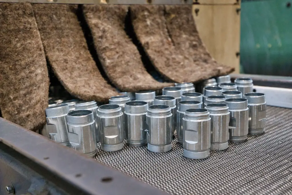 Metal parts on a conveyor belt in a vibratory finishing machine.