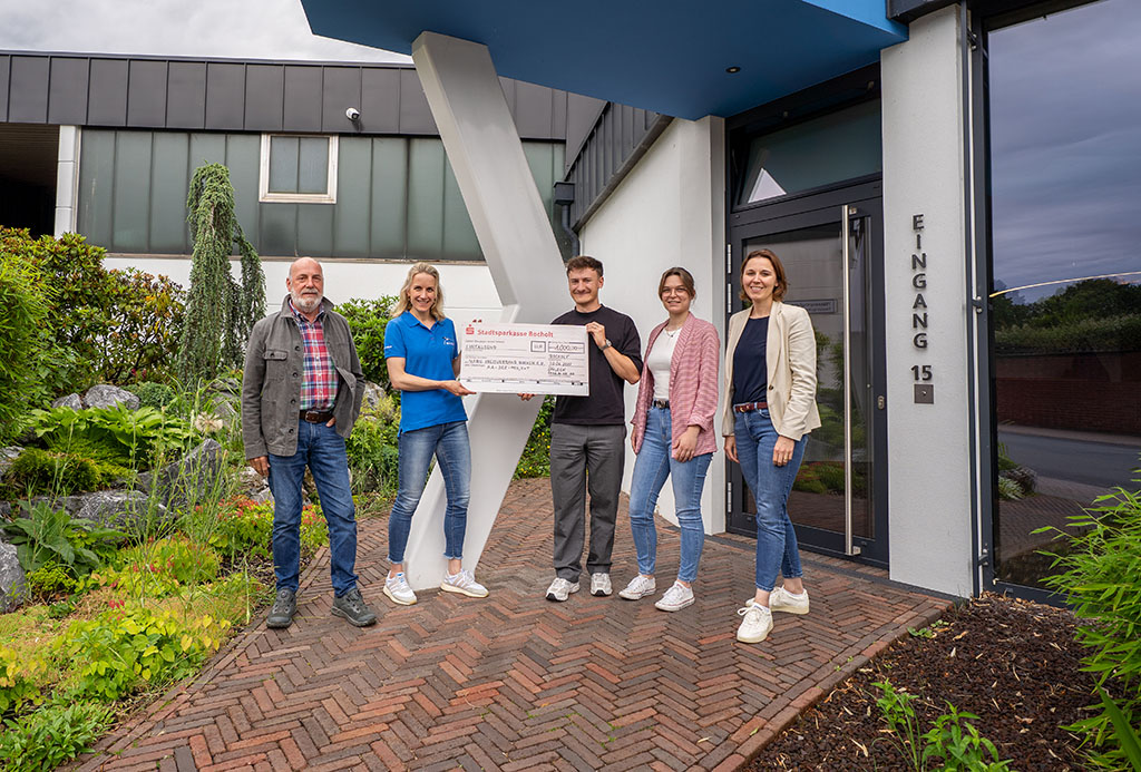 Three Spaleck employees present a donation check to two members of the NABU Borken District Association in front of Spaleck’s landscaped entrance in Bocholt