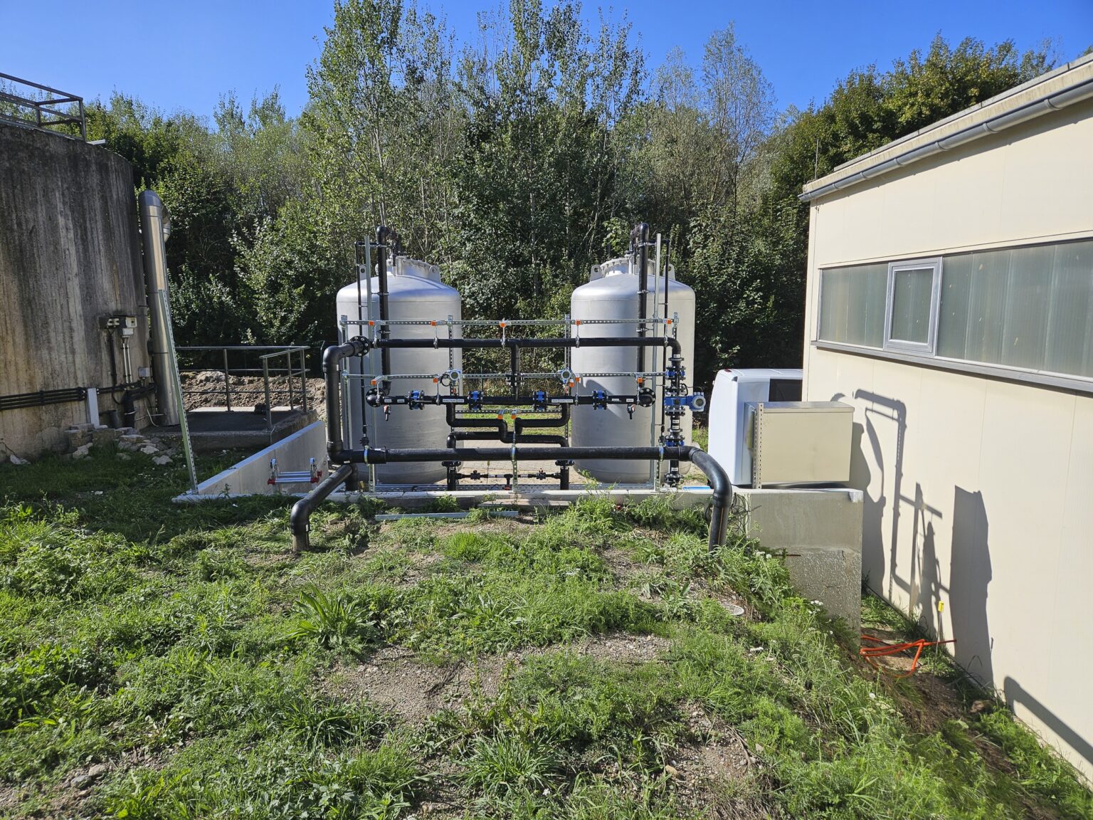 Two tanks for activated carbon filtration, along with the associated piping, next to a factory building.