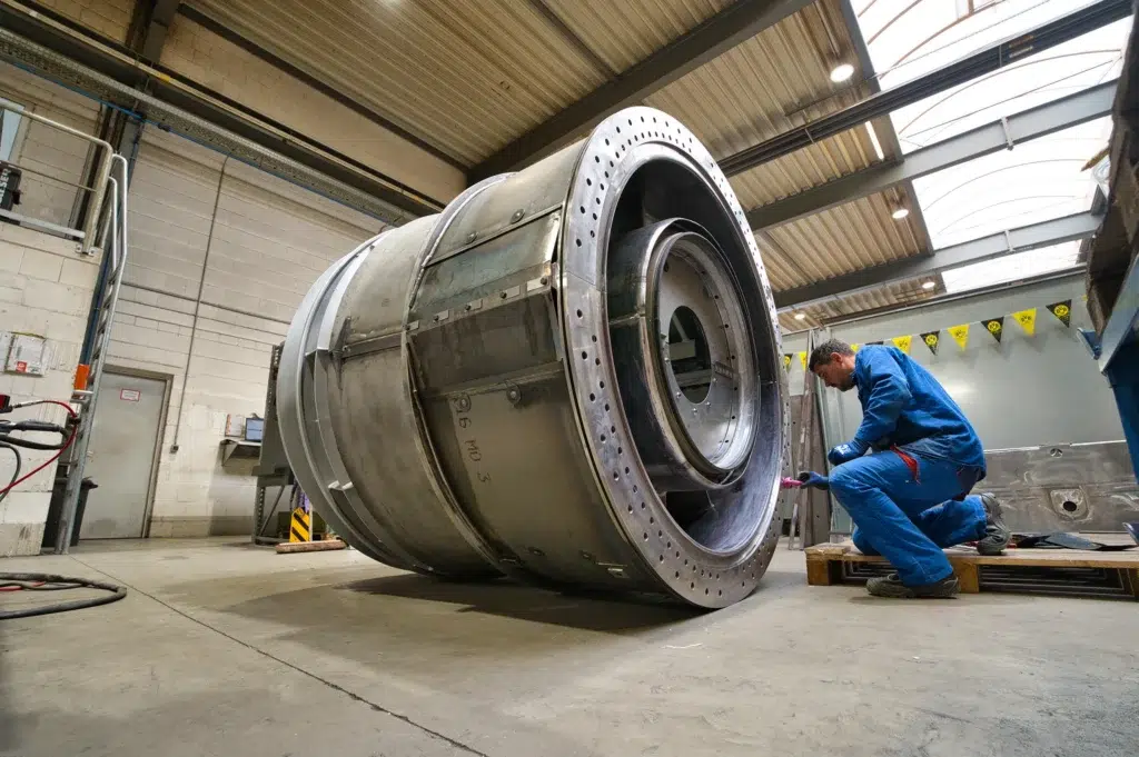 SPALECK, a construction mechanic, is kneeling next to a large welded assembly and installing parts. The assembly is part of a large welded assembly for a gas turbine. The photo shows production at SPALECK.