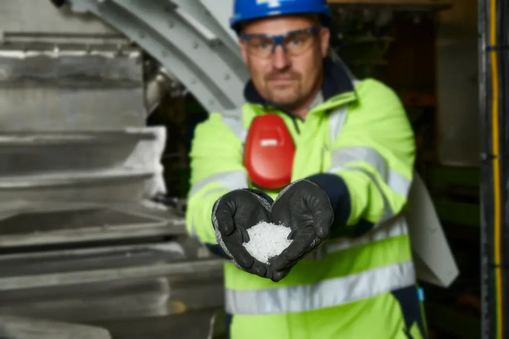 A production worker at a plastic pellet manufacturer holds freshly produced and screened pellets up to the camera