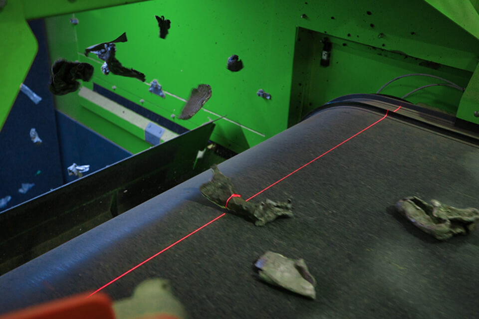 Metal parts on a conveyor belt in a recycling plant with a laser line