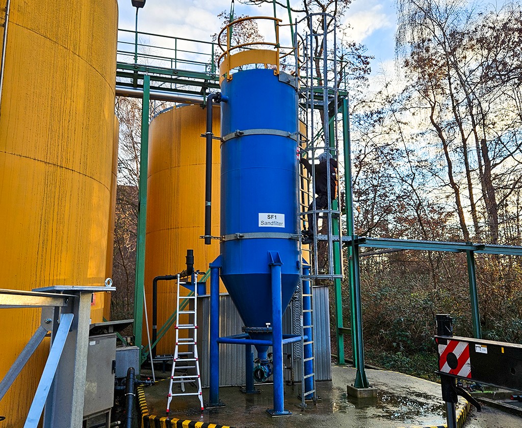 Blue tank for sand filtration in water treatment, next to yellow tanks.