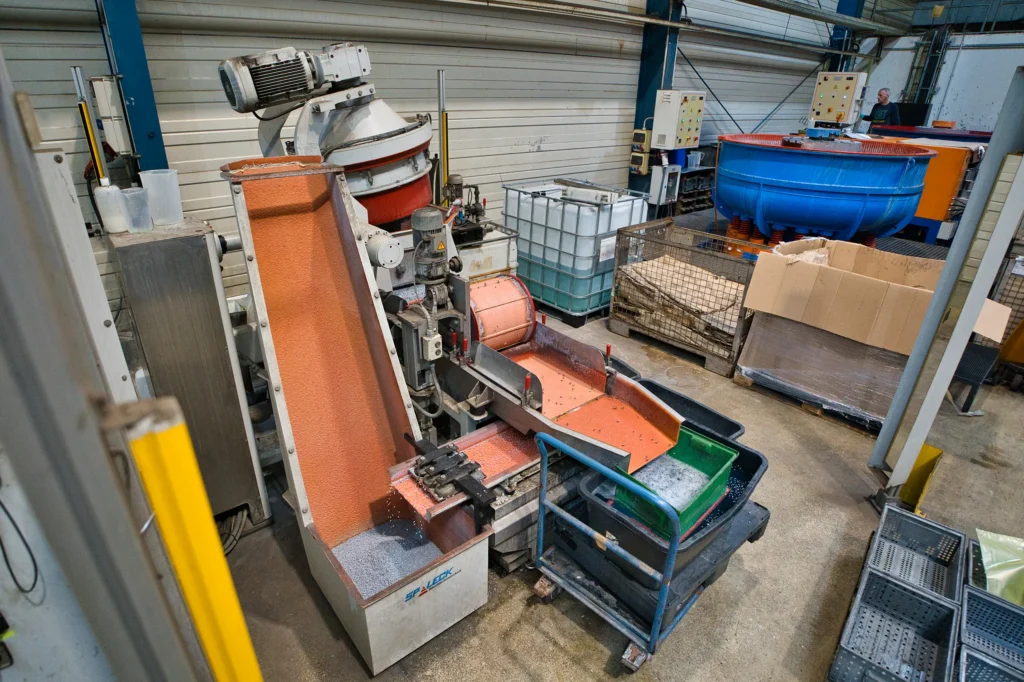 Industrial hall with a vibratory finishing machine and a blue drum in the background.