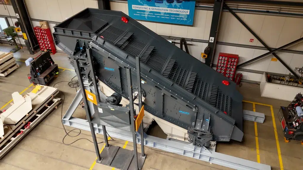 A view of a gray single-deck sieve machine standing on a light gray base frame. The recycling screen is currently in production at SPALECK and is used for processing bulky waste. It features SPALECK air suspension for screening machines and a screening deck optimized for bulky waste.