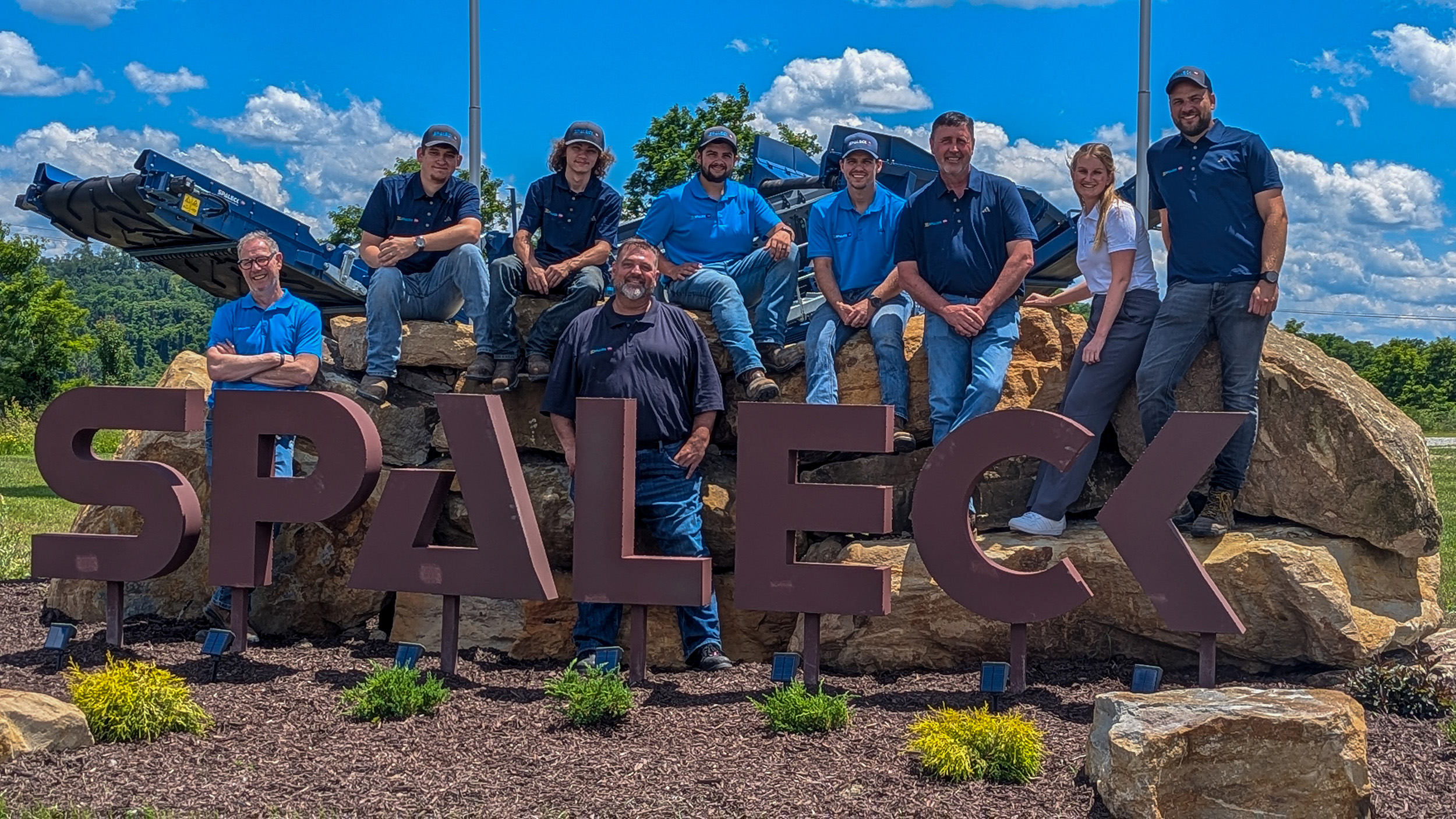 Team photo of Spaleck USA in front of the Spaleck logo in Charleroi at the site opening, with a blue sky in the background